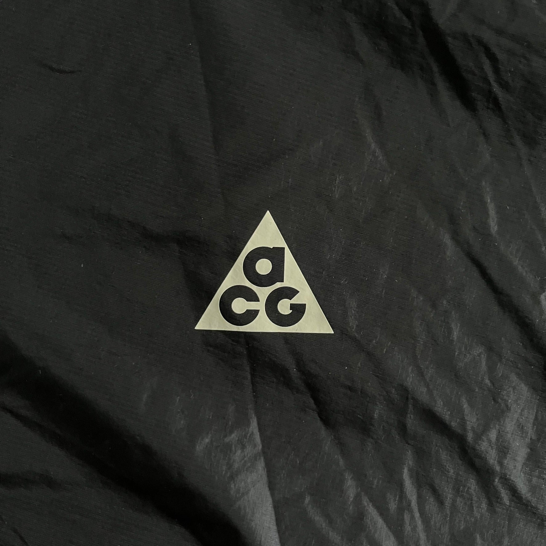 Nike ACG “Cinder Cone” Windbreaker in black, crafted from 100% recycled nylon ripstop. Features a lightweight, water-repellent shell, half-zip closure, and extended collar for added coverage. Designed with no shoulder seams for mobility and finished with printed ACG chest branding, two zippered pockets, and an internal baby carabiner.