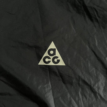 Nike ACG “Cinder Cone” Windbreaker in black, crafted from 100% recycled nylon ripstop. Features a lightweight, water-repellent shell, half-zip closure, and extended collar for added coverage. Designed with no shoulder seams for mobility and finished with printed ACG chest branding, two zippered pockets, and an internal baby carabiner.