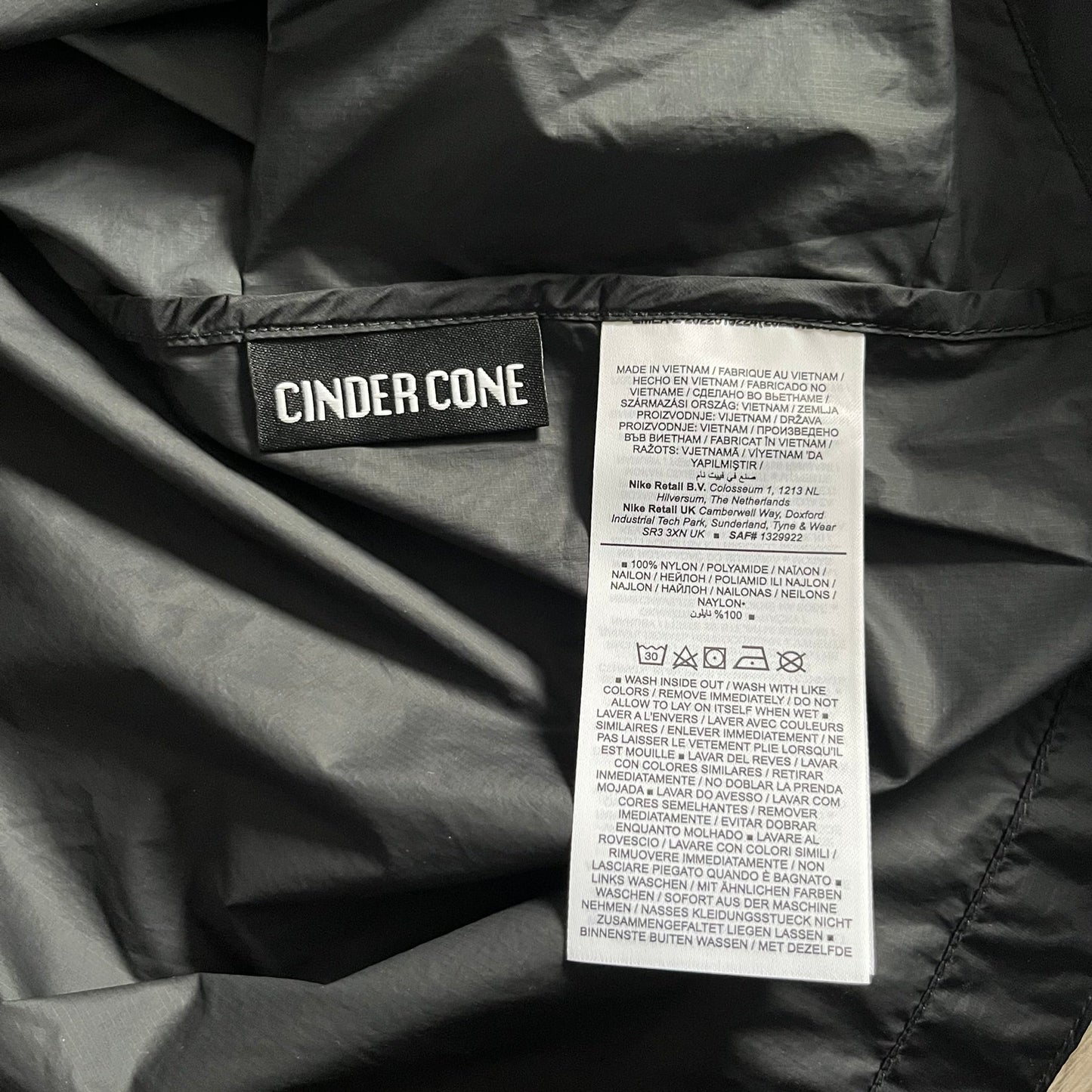 Nike ACG “Cinder Cone” Windbreaker in black, crafted from 100% recycled nylon ripstop. Features a lightweight, water-repellent shell, half-zip closure, and extended collar for added coverage. Designed with no shoulder seams for mobility and finished with printed ACG chest branding, two zippered pockets, and an internal baby carabiner.