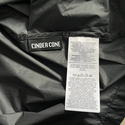 Nike ACG “Cinder Cone” Windbreaker in black, crafted from 100% recycled nylon ripstop. Features a lightweight, water-repellent shell, half-zip closure, and extended collar for added coverage. Designed with no shoulder seams for mobility and finished with printed ACG chest branding, two zippered pockets, and an internal baby carabiner.