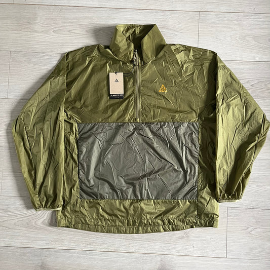 Olive Nike ACG Cinder Cone 1/2 Zip Jacket made from durable nylon ripstop with water-repellent finish. Designed with no shoulder seams for mobility, elastic cuffs, reinforced hem, and two zip pockets. Includes printed chest logo and internal ACG carabiner, with packable oversized construction.