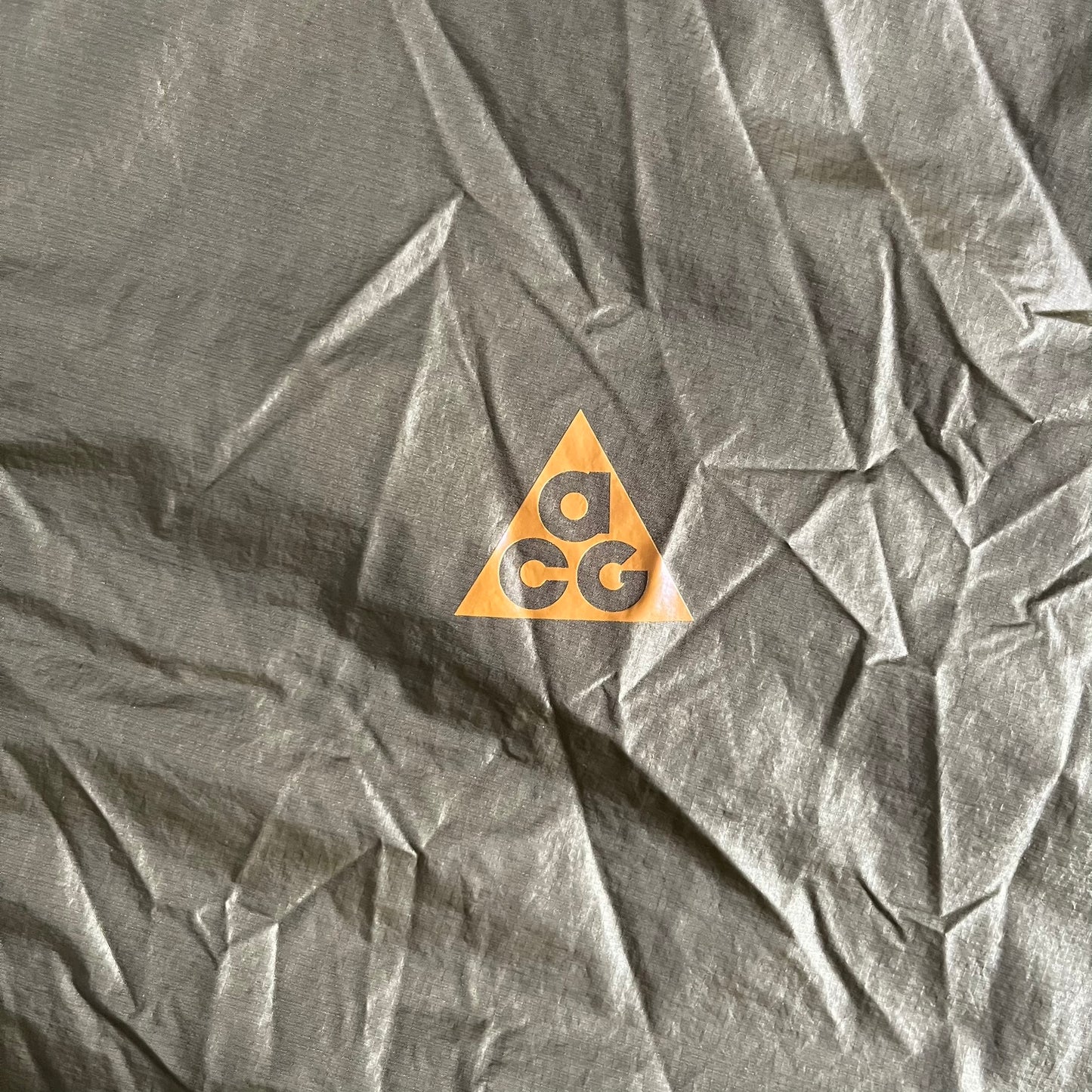 Olive Nike ACG Cinder Cone 1/2 Zip Jacket made from durable nylon ripstop with water-repellent finish. Designed with no shoulder seams for mobility, elastic cuffs, reinforced hem, and two zip pockets. Includes printed chest logo and internal ACG carabiner, with packable oversized construction.