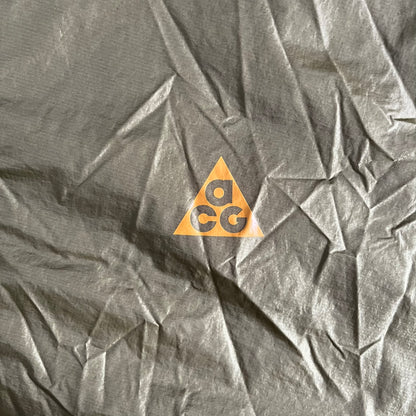 Olive Nike ACG Cinder Cone 1/2 Zip Jacket made from durable nylon ripstop with water-repellent finish. Designed with no shoulder seams for mobility, elastic cuffs, reinforced hem, and two zip pockets. Includes printed chest logo and internal ACG carabiner, with packable oversized construction.