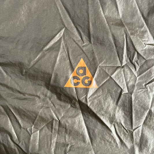 Olive Nike ACG Cinder Cone 1/2 Zip Jacket made from durable nylon ripstop with water-repellent finish. Designed with no shoulder seams for mobility, elastic cuffs, reinforced hem, and two zip pockets. Includes printed chest logo and internal ACG carabiner, with packable oversized construction.