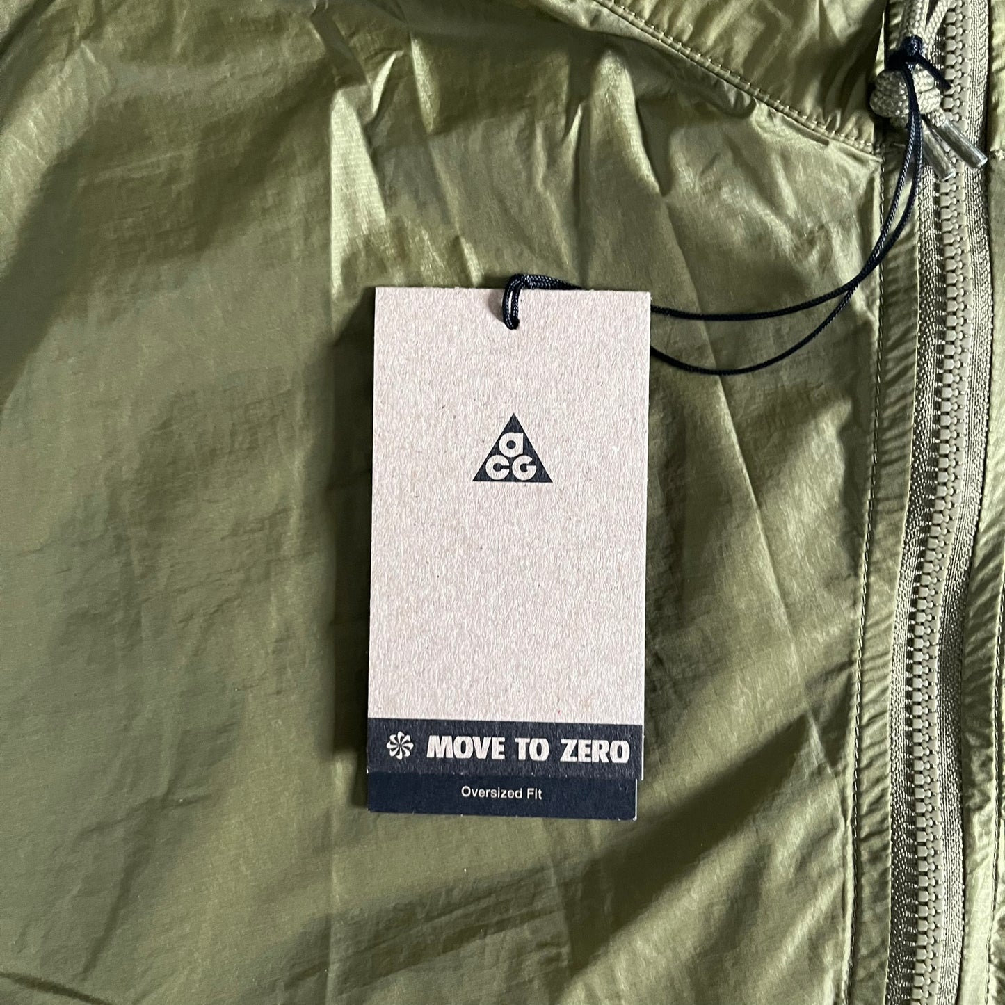 Olive Nike ACG Cinder Cone 1/2 Zip Jacket made from durable nylon ripstop with water-repellent finish. Designed with no shoulder seams for mobility, elastic cuffs, reinforced hem, and two zip pockets. Includes printed chest logo and internal ACG carabiner, with packable oversized construction.