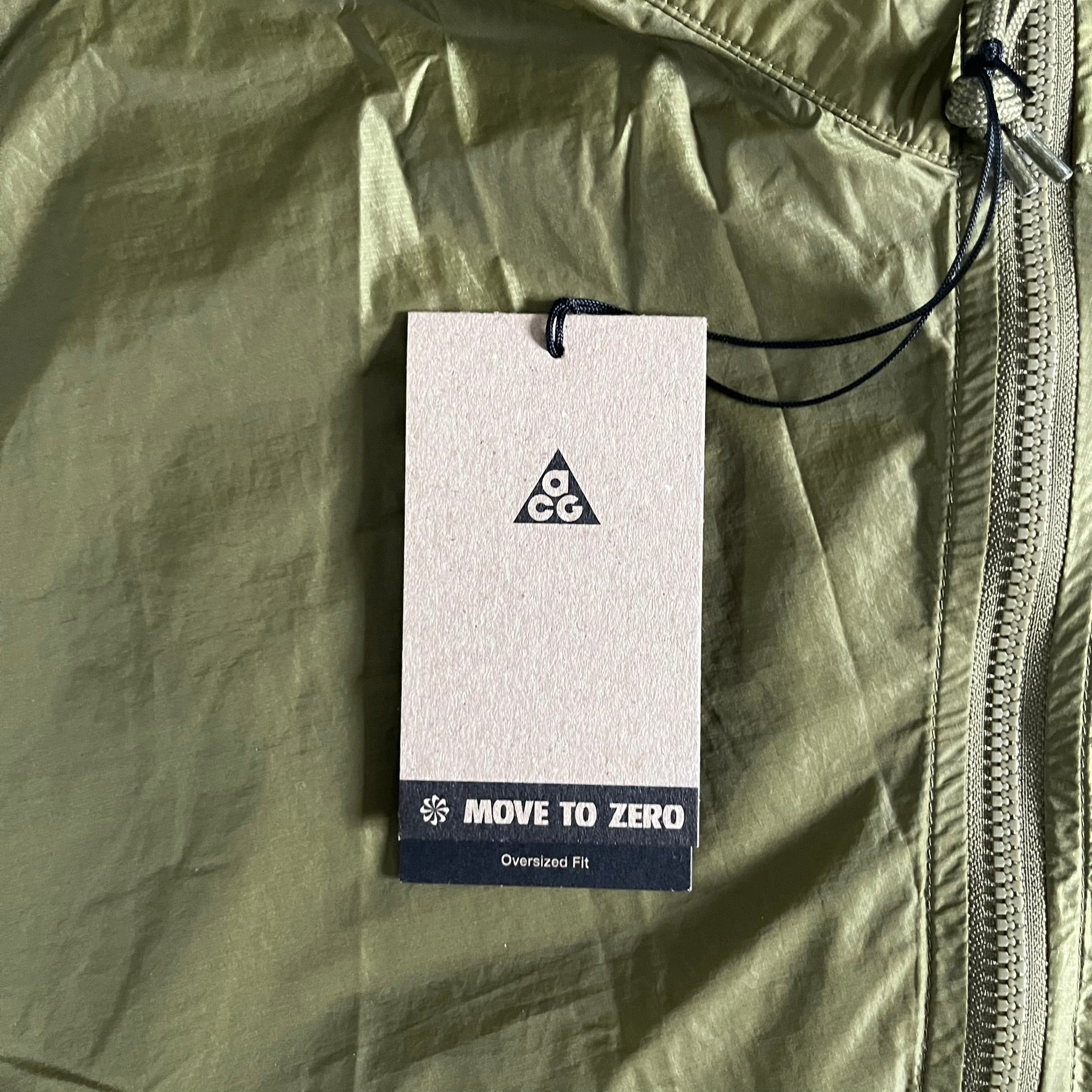 Olive Nike ACG Cinder Cone 1/2 Zip Jacket made from durable nylon ripstop with water-repellent finish. Designed with no shoulder seams for mobility, elastic cuffs, reinforced hem, and two zip pockets. Includes printed chest logo and internal ACG carabiner, with packable oversized construction.