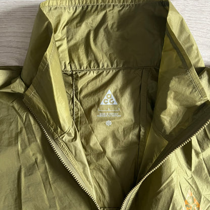 Olive Nike ACG Cinder Cone 1/2 Zip Jacket made from durable nylon ripstop with water-repellent finish. Designed with no shoulder seams for mobility, elastic cuffs, reinforced hem, and two zip pockets. Includes printed chest logo and internal ACG carabiner, with packable oversized construction.