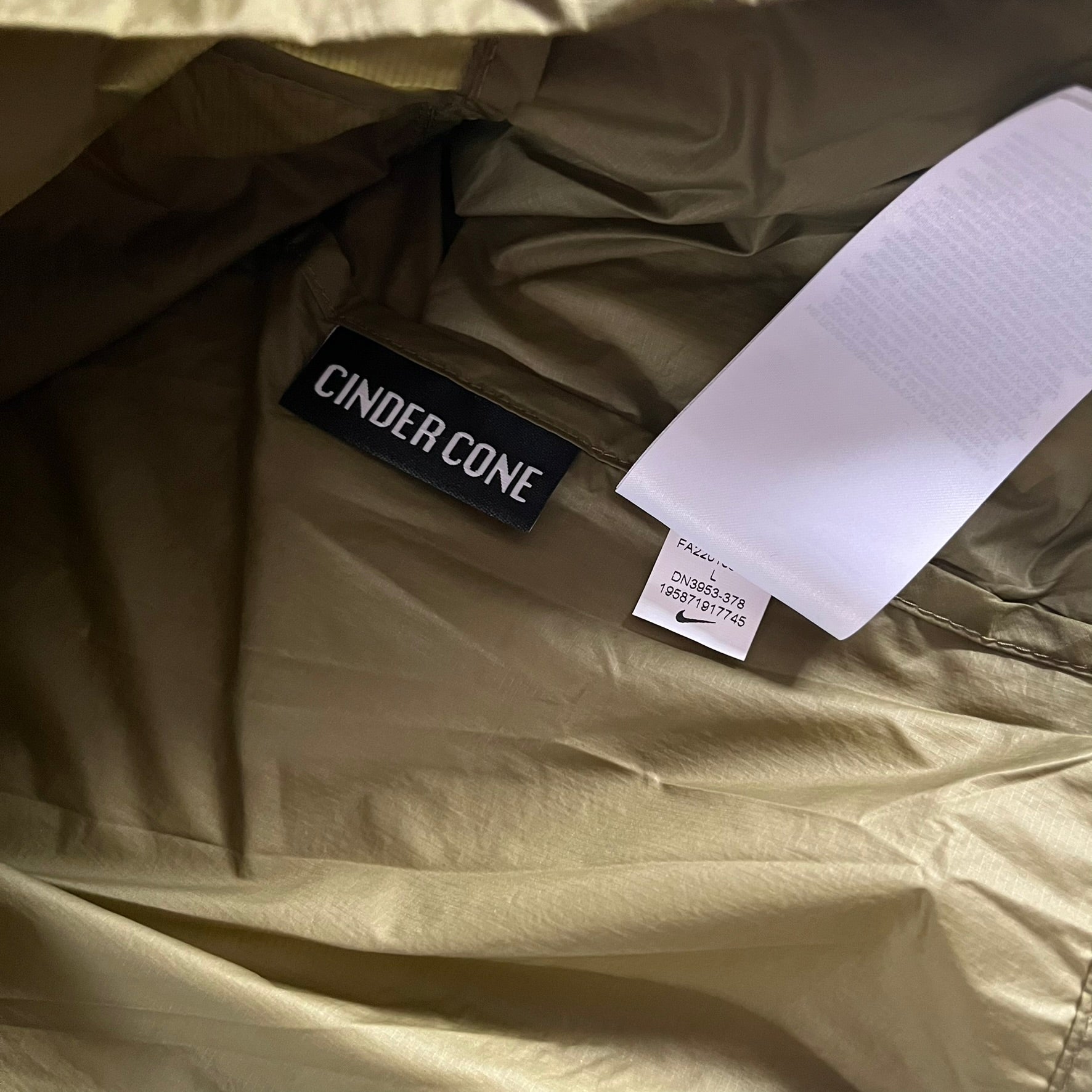Olive Nike ACG Cinder Cone 1/2 Zip Jacket made from durable nylon ripstop with water-repellent finish. Designed with no shoulder seams for mobility, elastic cuffs, reinforced hem, and two zip pockets. Includes printed chest logo and internal ACG carabiner, with packable oversized construction.