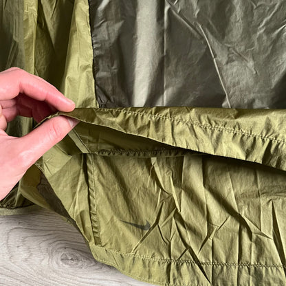 Olive Nike ACG Cinder Cone 1/2 Zip Jacket made from durable nylon ripstop with water-repellent finish. Designed with no shoulder seams for mobility, elastic cuffs, reinforced hem, and two zip pockets. Includes printed chest logo and internal ACG carabiner, with packable oversized construction.