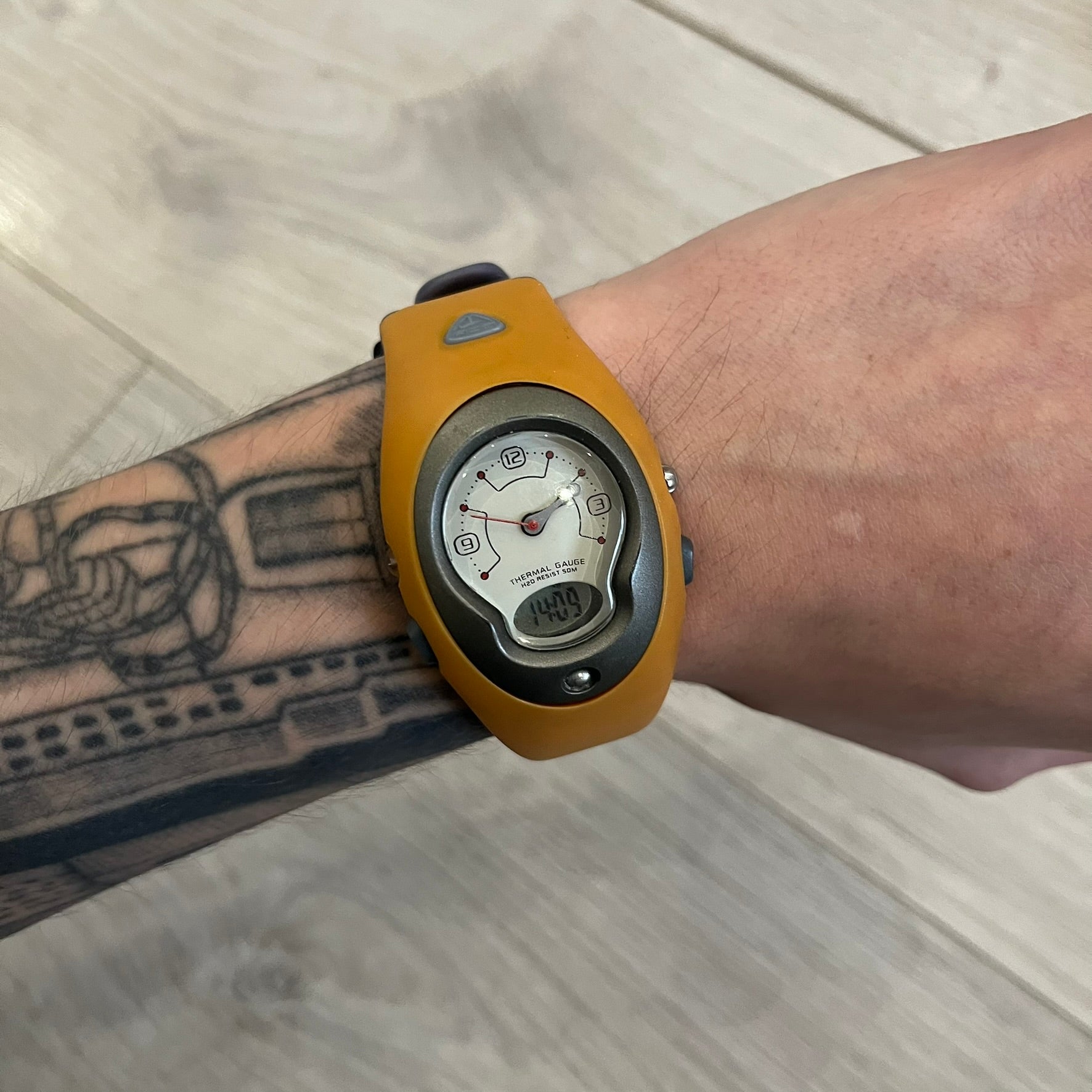 Nike ACG Thermal Gauge Watch featuring an ani-digi display with temperature, date, timer, alarm, and counter functions. Designed with a durable stainless-steel and plastic build, a white dial with grey outline, and an orange strap with the ACG logo. Water-resistant up to 50m, this Nike ACG outdoor watch blends utility with signature 90s–2000s adventure styling.