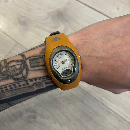 Nike ACG Thermal Gauge Watch featuring an ani-digi display with temperature, date, timer, alarm, and counter functions. Designed with a durable stainless-steel and plastic build, a white dial with grey outline, and an orange strap with the ACG logo. Water-resistant up to 50m, this Nike ACG outdoor watch blends utility with signature 90s–2000s adventure styling.