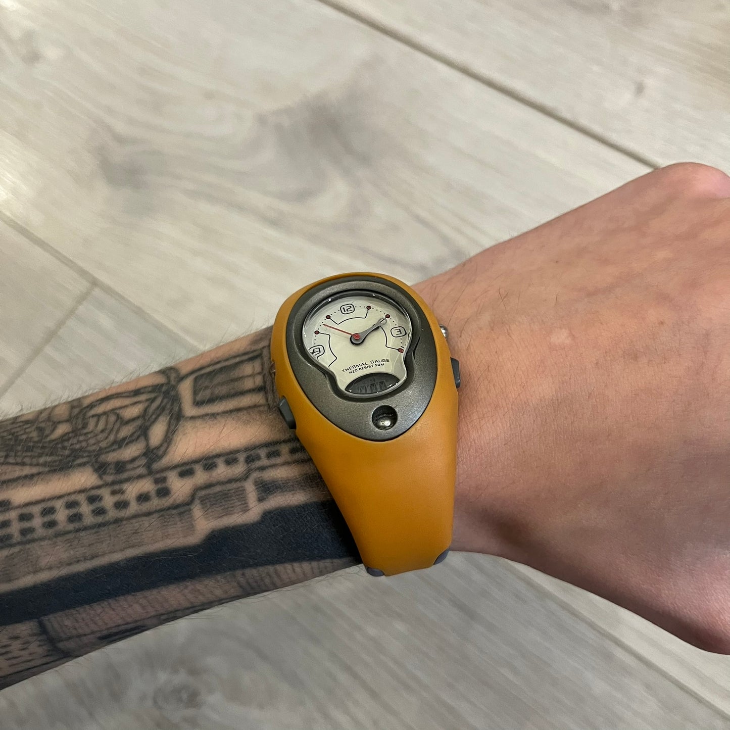 Nike ACG Thermal Gauge Watch featuring an ani-digi display with temperature, date, timer, alarm, and counter functions. Designed with a durable stainless-steel and plastic build, a white dial with grey outline, and an orange strap with the ACG logo. Water-resistant up to 50m, this Nike ACG outdoor watch blends utility with signature 90s–2000s adventure styling.