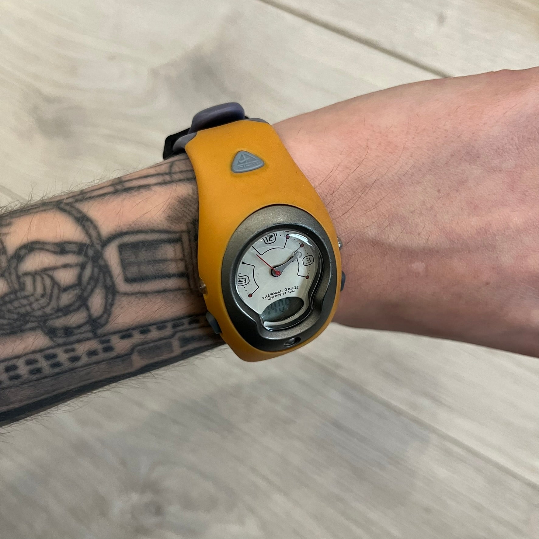 Nike ACG Thermal Gauge Watch featuring an ani-digi display with temperature, date, timer, alarm, and counter functions. Designed with a durable stainless-steel and plastic build, a white dial with grey outline, and an orange strap with the ACG logo. Water-resistant up to 50m, this Nike ACG outdoor watch blends utility with signature 90s–2000s adventure styling.