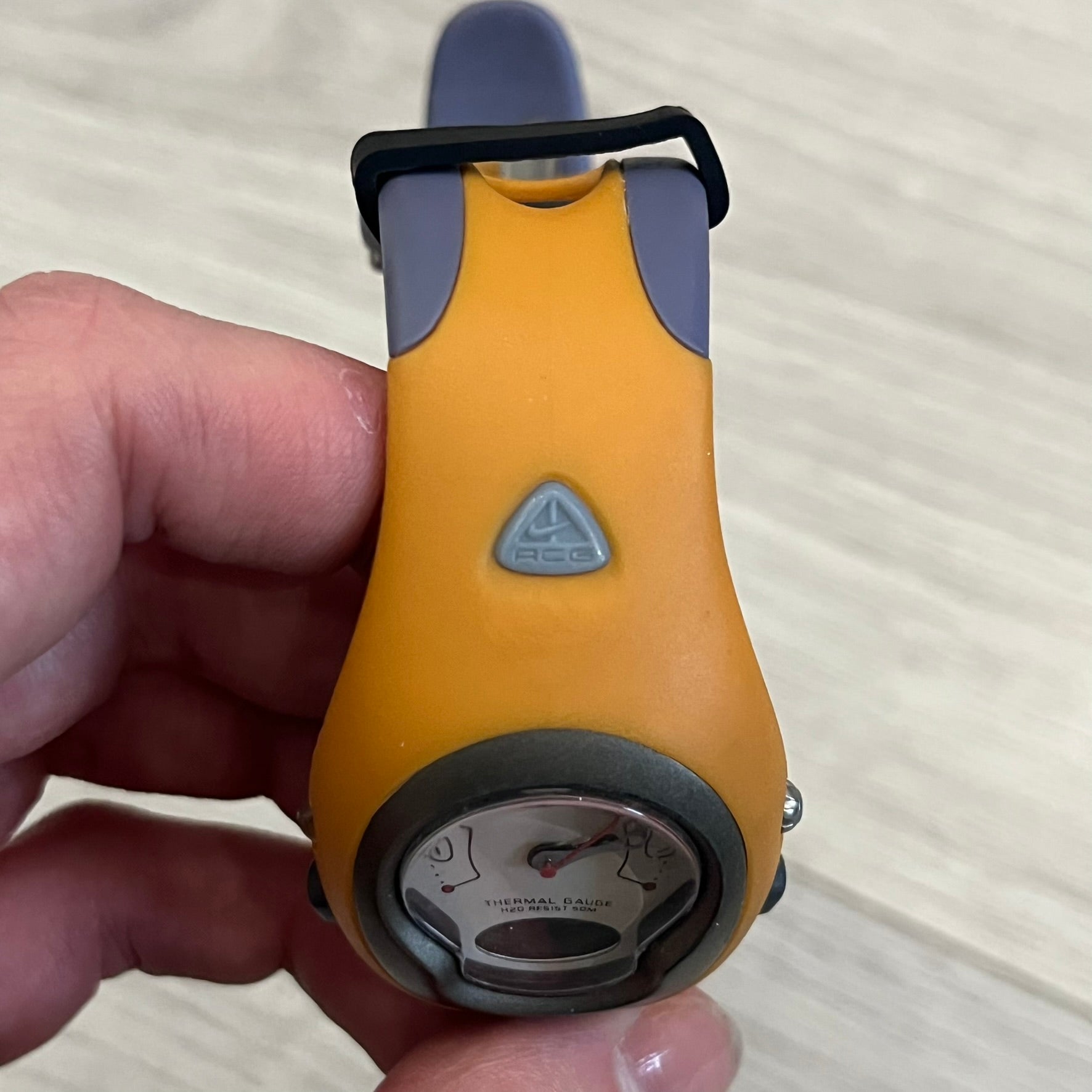 Nike ACG Thermal Gauge Watch featuring an ani-digi display with temperature, date, timer, alarm, and counter functions. Designed with a durable stainless-steel and plastic build, a white dial with grey outline, and an orange strap with the ACG logo. Water-resistant up to 50m, this Nike ACG outdoor watch blends utility with signature 90s–2000s adventure styling.