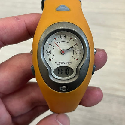 Nike ACG Thermal Gauge Watch featuring an ani-digi display with temperature, date, timer, alarm, and counter functions. Designed with a durable stainless-steel and plastic build, a white dial with grey outline, and an orange strap with the ACG logo. Water-resistant up to 50m, this Nike ACG outdoor watch blends utility with signature 90s–2000s adventure styling.