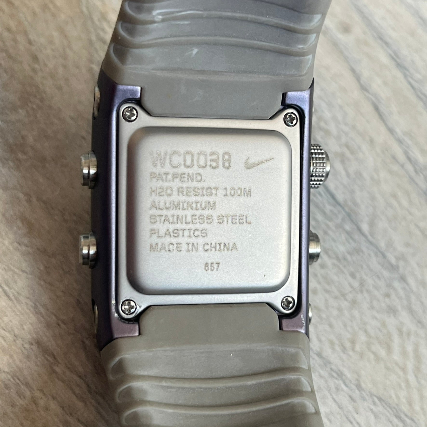 Nike Anvil Comold Reg Digital Watch WC0038 is a digital wristwatch featuring a dark purple/violet aluminum and stainless steel case with a white-outlined display. The watch includes four side buttons, a digital screen, and grey rubber straps, constructed from a mix of aluminum, stainless steel, and plastic. It is water resistant up to 100 meters, powered by fresh batteries, and comes with the original box.