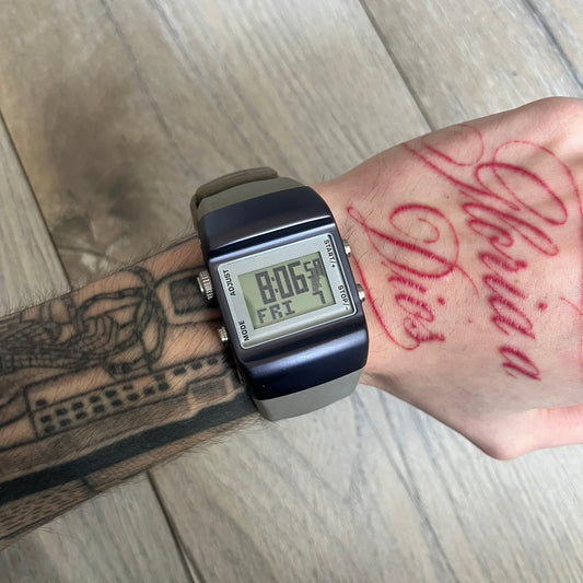 Nike Anvil Comold Reg Digital Watch WC0038 is a digital wristwatch featuring a dark purple/violet aluminum and stainless steel case with a white-outlined display. The watch includes four side buttons, a digital screen, and grey rubber straps, constructed from a mix of aluminum, stainless steel, and plastic. It is water resistant up to 100 meters, powered by fresh batteries, and comes with the original box.