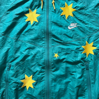 Nike 2008 Australia Olympics Split Windbreaker in teal, detailed with yellow star embroidery inspired by Australia’s national emblem. Designed with double side zippers that let the jacket separate for modular wear. Includes embroidered white Nike logo on the chest and Australian flag details inside both pockets.