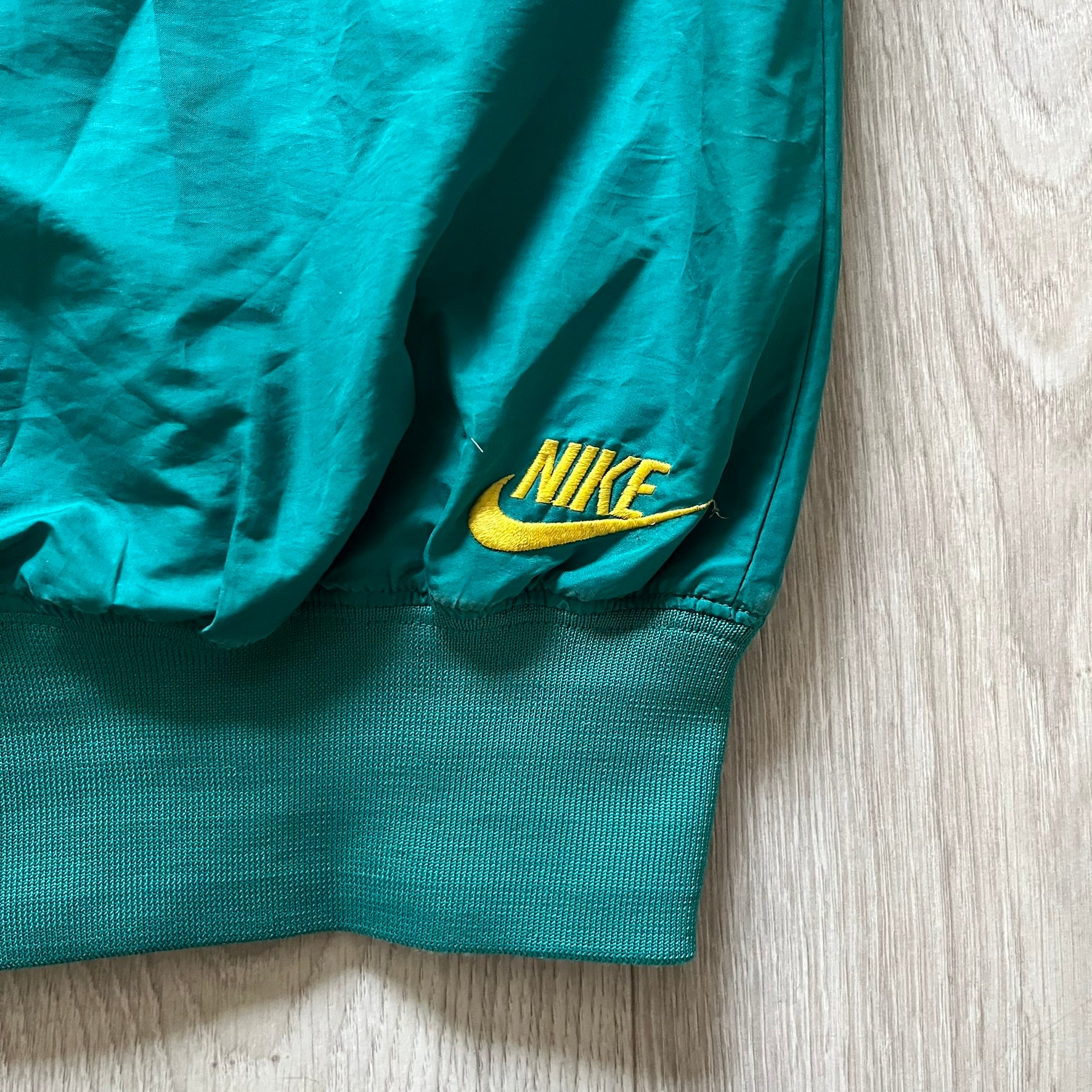 Nike 2008 Australia Olympics Split Windbreaker in teal, detailed with yellow star embroidery inspired by Australia’s national emblem. Designed with double side zippers that let the jacket separate for modular wear. Includes embroidered white Nike logo on the chest and Australian flag details inside both pockets.