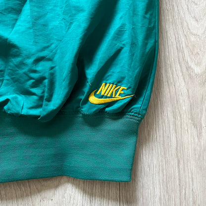 Nike 2008 Australia Olympics Split Windbreaker in teal, detailed with yellow star embroidery inspired by Australia’s national emblem. Designed with double side zippers that let the jacket separate for modular wear. Includes embroidered white Nike logo on the chest and Australian flag details inside both pockets.