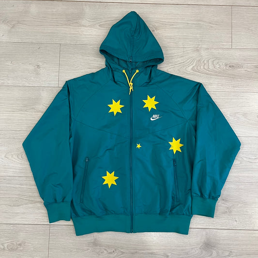 Nike 2008 Australia Olympics Split Windbreaker in teal, detailed with yellow star embroidery inspired by Australia’s national emblem. Designed with double side zippers that let the jacket separate for modular wear. Includes embroidered white Nike logo on the chest and Australian flag details inside both pockets.