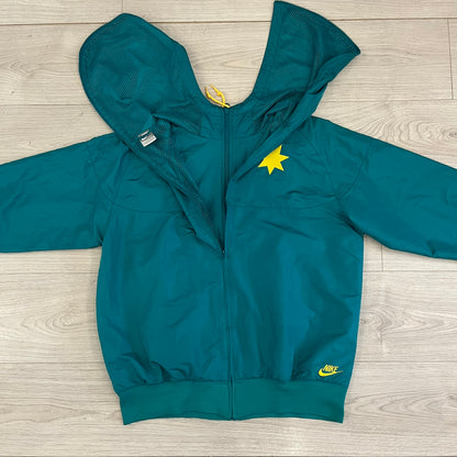 Nike 2008 Australia Olympics Split Windbreaker in teal, detailed with yellow star embroidery inspired by Australia’s national emblem. Designed with double side zippers that let the jacket separate for modular wear. Includes embroidered white Nike logo on the chest and Australian flag details inside both pockets.
