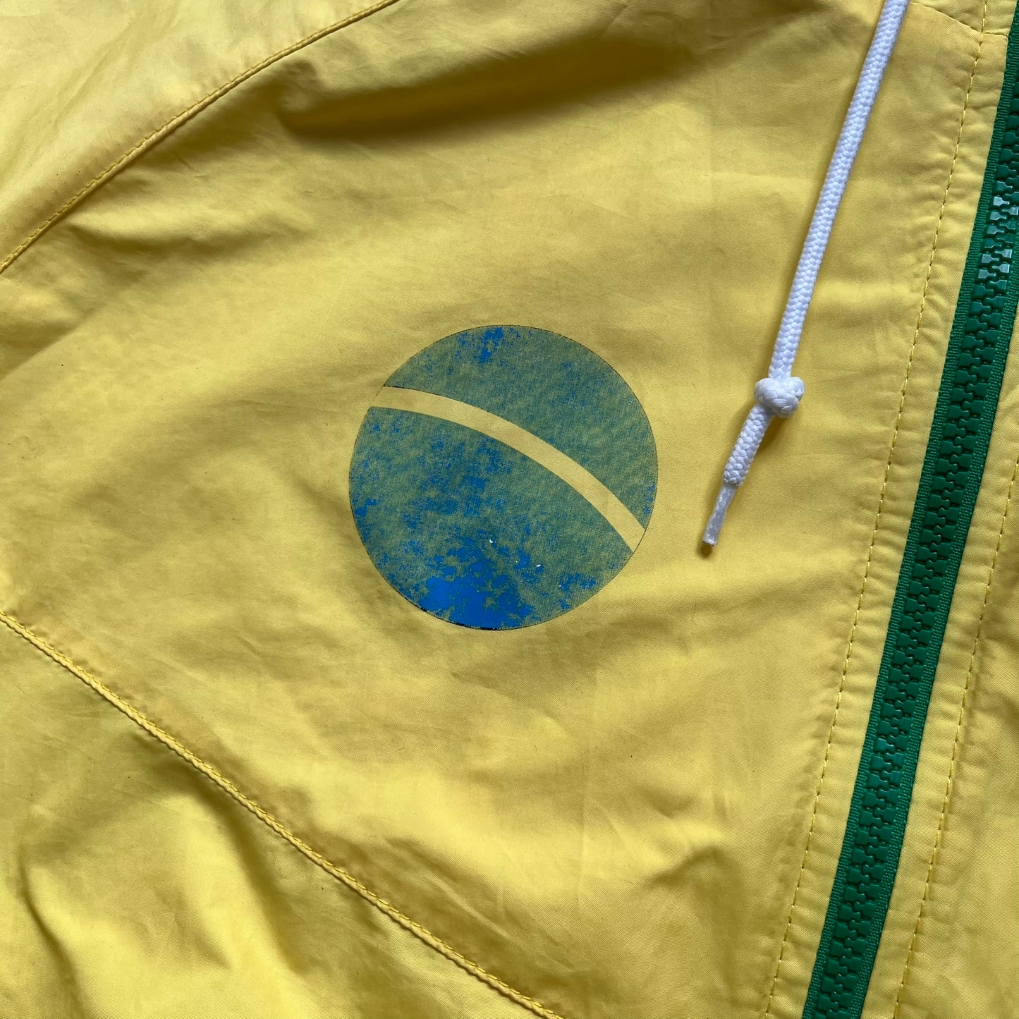 Nike Brazil Olympics Split Windbreaker from 2008, created by designer Jarrett Reynolds. Crafted in yellow with green hems and zippers. Blue circle and white Nike embroidered logo on the chest. This innovative jacket can be zipped apart on both sides and merged with other compatible models. Hidden inside, a small Brazil flags accent completes the concept.