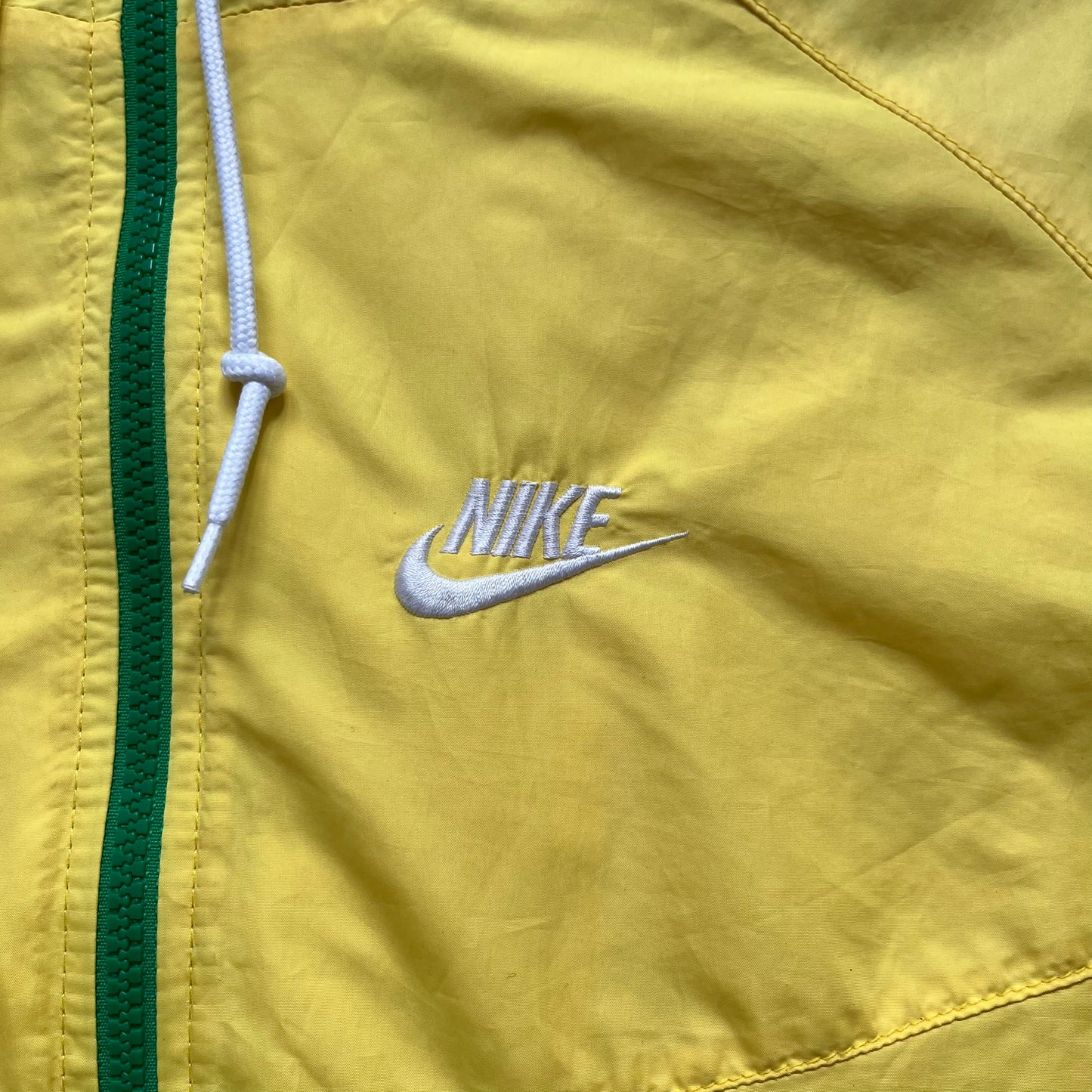 Nike Brazil Olympics Split Windbreaker from 2008, created by designer Jarrett Reynolds. Crafted in yellow with green hems and zippers. Blue circle and white Nike embroidered logo on the chest. This innovative jacket can be zipped apart on both sides and merged with other compatible models. Hidden inside, a small Brazil flags accent completes the concept.