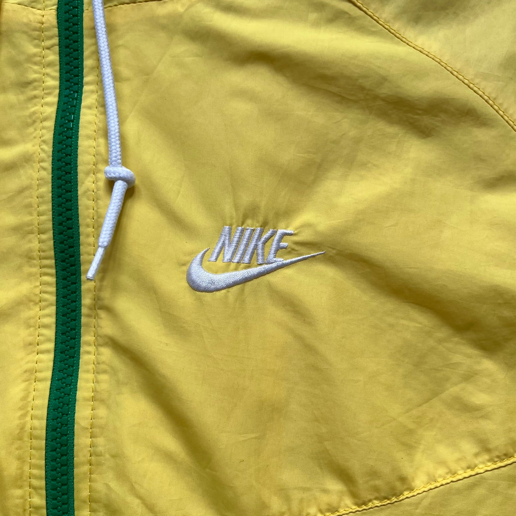 Nike Brazil Olympics Split Windbreaker from 2008, created by designer Jarrett Reynolds. Crafted in yellow with green hems and zippers. Blue circle and white Nike embroidered logo on the chest. This innovative jacket can be zipped apart on both sides and merged with other compatible models. Hidden inside, a small Brazil flags accent completes the concept.