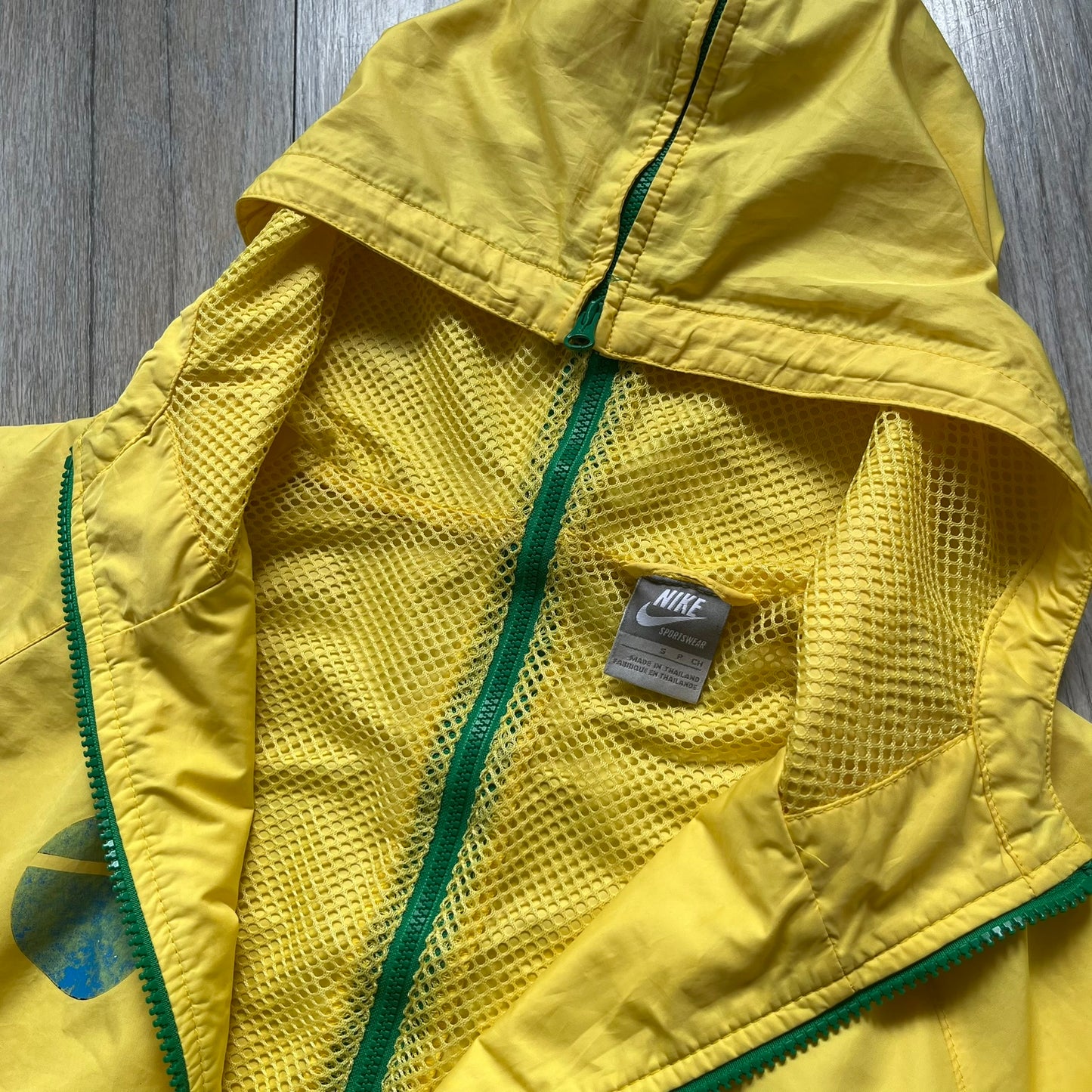 Nike Brazil Olympics Split Windbreaker from 2008, created by designer Jarrett Reynolds. Crafted in yellow with green hems and zippers. Blue circle and white Nike embroidered logo on the chest. This innovative jacket can be zipped apart on both sides and merged with other compatible models. Hidden inside, a small Brazil flags accent completes the concept.