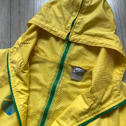 Nike Brazil Olympics Split Windbreaker from 2008, created by designer Jarrett Reynolds. Crafted in yellow with green hems and zippers. Blue circle and white Nike embroidered logo on the chest. This innovative jacket can be zipped apart on both sides and merged with other compatible models. Hidden inside, a small Brazil flags accent completes the concept.