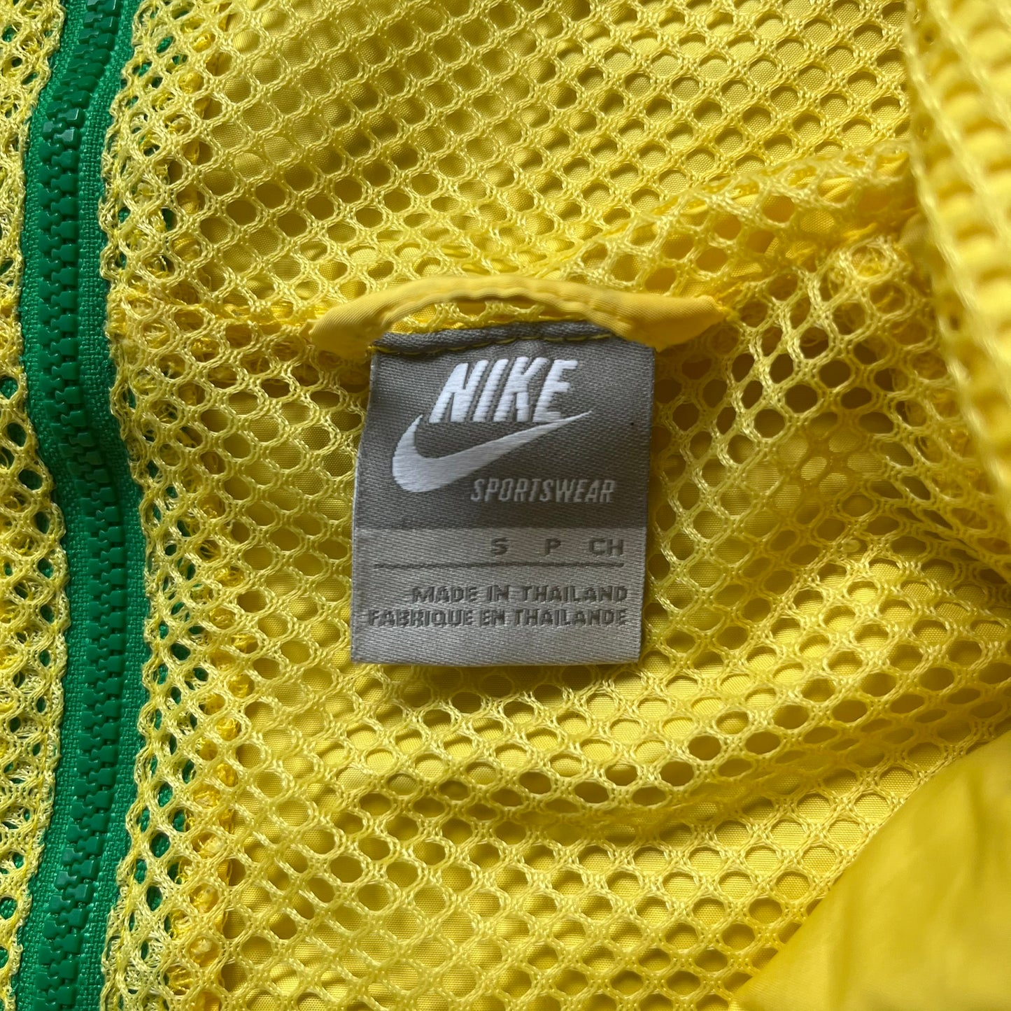 Nike Brazil Olympics Split Windbreaker from 2008, created by designer Jarrett Reynolds. Crafted in yellow with green hems and zippers. Blue circle and white Nike embroidered logo on the chest. This innovative jacket can be zipped apart on both sides and merged with other compatible models. Hidden inside, a small Brazil flags accent completes the concept.