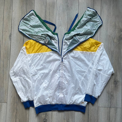 Nike Brazil windbreaker released in 2008 to mark the 50th anniversary of Brazil’s football legacy. Features a split color-block design with white lower panels and sleeves, yellow and green upper section, blue cuffs and hems, and a green hood. Detailed with a gold embroidered Nike logo on the chest, a gold-tone metal Brazil crest pin on the opposite side, and “1958-2008” with a “50” printed on the hood. The hood interior is white with an all-over green star pattern.