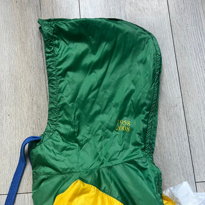 Nike Brazil windbreaker released in 2008 to mark the 50th anniversary of Brazil’s football legacy. Features a split color-block design with white lower panels and sleeves, yellow and green upper section, blue cuffs and hems, and a green hood. Detailed with a gold embroidered Nike logo on the chest, a gold-tone metal Brazil crest pin on the opposite side, and “1958-2008” with a “50” printed on the hood. The hood interior is white with an all-over green star pattern.