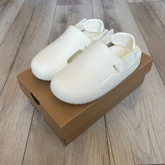 Nike Calm Mule Wmns White Sandals FB2185-100 are women’s slip-on mules finished in a Sail/White colorway, constructed from a single-piece foam upper for a seamless design. The model features water-resistant, easy-to-clean foam with a textured footbed and full-length rubber outsole for traction on wet surfaces. An adjustable and removable heel strap allows for a customizable fit, while side openings provide ventilation.