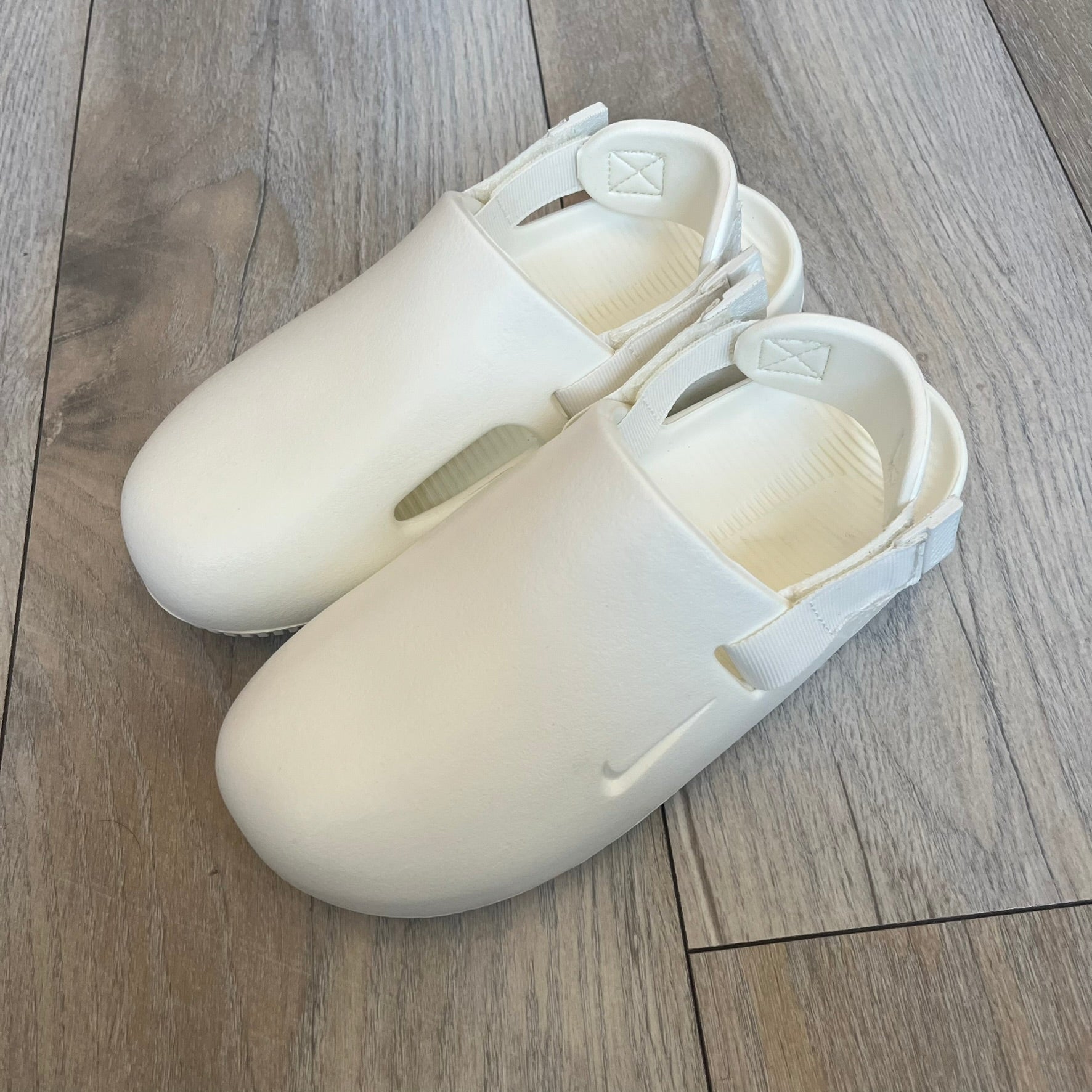 Nike Calm Mule Wmns White Sandals FB2185-100 are women’s slip-on mules finished in a Sail/White colorway, constructed from a single-piece foam upper for a seamless design. The model features water-resistant, easy-to-clean foam with a textured footbed and full-length rubber outsole for traction on wet surfaces. An adjustable and removable heel strap allows for a customizable fit, while side openings provide ventilation.