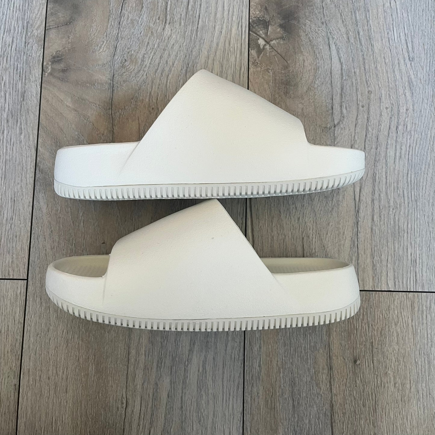 Nike Calm Wmns “Sail” Slide Sandals are women’s slip-on slides released in 2023, featuring a monochromatic Sail/White colorway and a one-piece foam construction. The design includes a contoured footbed with textured detailing for grip, a waterproof outer shell, and a midfoot strap with a debossed Nike Swoosh logo. A full rubber outsole provides durable traction, making this model suitable for everyday wear and wet conditions.