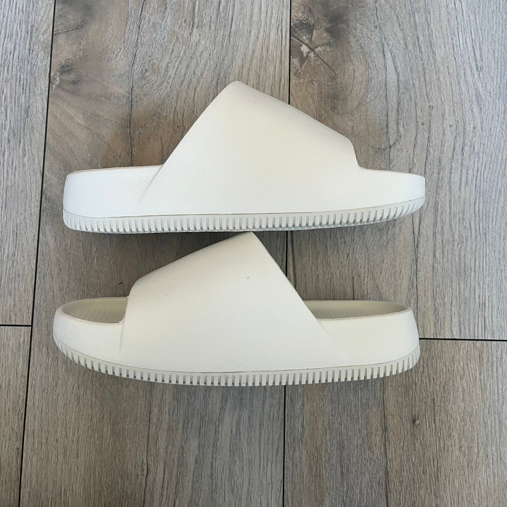 Nike Calm Wmns “Sail” Slide Sandals are women’s slip-on slides released in 2023, featuring a monochromatic Sail/White colorway and a one-piece foam construction. The design includes a contoured footbed with textured detailing for grip, a waterproof outer shell, and a midfoot strap with a debossed Nike Swoosh logo. A full rubber outsole provides durable traction, making this model suitable for everyday wear and wet conditions.