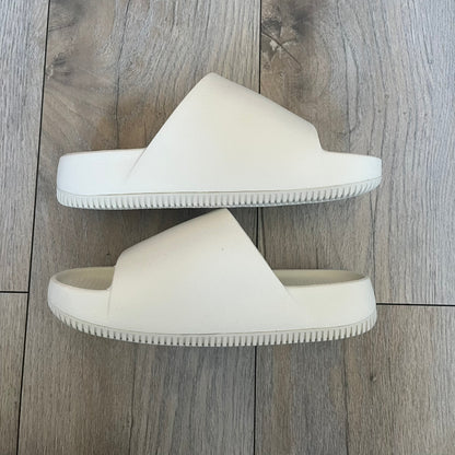 Nike Calm Wmns “Sail” Slide Sandals are women’s slip-on slides released in 2023, featuring a monochromatic Sail/White colorway and a one-piece foam construction. The design includes a contoured footbed with textured detailing for grip, a waterproof outer shell, and a midfoot strap with a debossed Nike Swoosh logo. A full rubber outsole provides durable traction, making this model suitable for everyday wear and wet conditions.