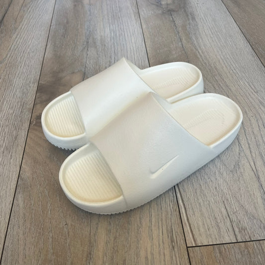 Nike Calm Wmns “Sail” Slide Sandals are women’s slip-on slides released in 2023, featuring a monochromatic Sail/White colorway and a one-piece foam construction. The design includes a contoured footbed with textured detailing for grip, a waterproof outer shell, and a midfoot strap with a debossed Nike Swoosh logo. A full rubber outsole provides durable traction, making this model suitable for everyday wear and wet conditions.