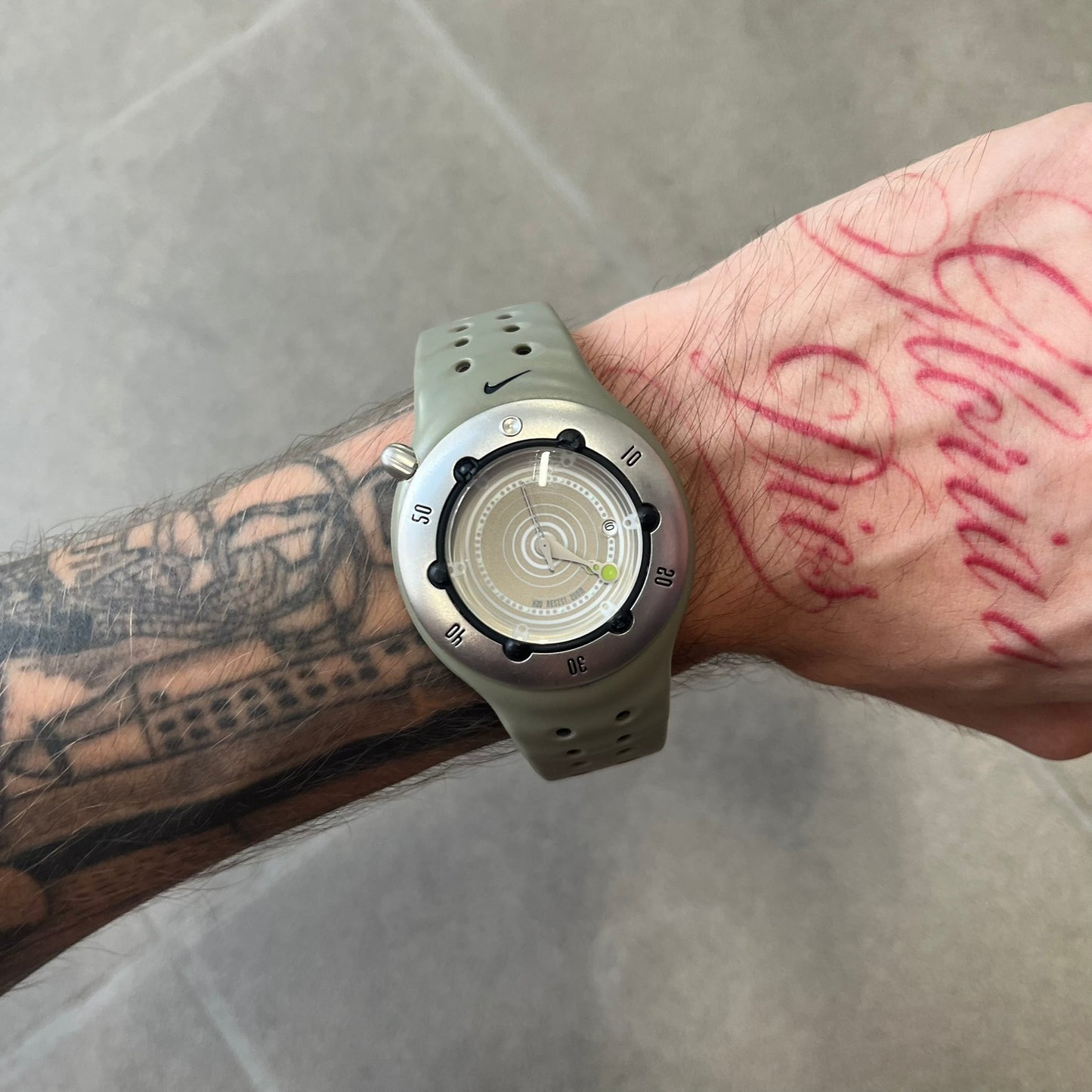 Nike Cayman WW0006 Dive Analog Watch features a grey polyurethane/rubber strap, silver rotating dive bezel, and a grey and white analog dial. It has a Japanese quartz movement, date indicator, luminous hands and hour markers, and 200-meter water resistance.
