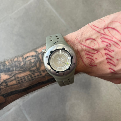Nike Cayman WW0006 Dive Analog Watch features a grey polyurethane/rubber strap, silver rotating dive bezel, and a grey and white analog dial. It has a Japanese quartz movement, date indicator, luminous hands and hour markers, and 200-meter water resistance.
