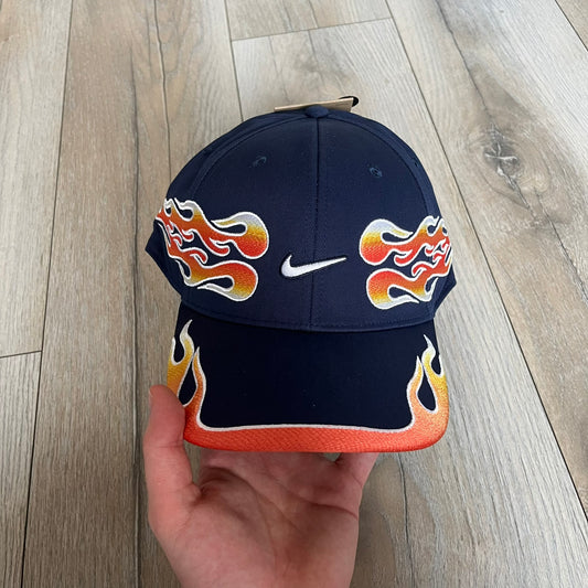 Nike Club Semi-Structured OG Midnight Navy Flame Cap is a navy baseball cap featuring a white Nike Swoosh centered on the front panel. Embroidered flame graphics in orange, yellow, and red extend across the front of the visor and side panels. A small white Nike Swoosh is placed at the back. The design is identified by code IH9258-410.