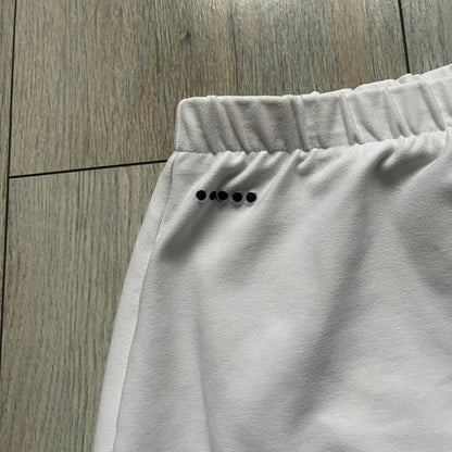 Nike Court Black Trim 90’s Tennis Skirt is a white women’s tennis skort with built-in inner shorts. It features a small Nike Court logo at the lower right hem and black trim detailing along the skirt hem and the bottom of the inner shorts legs.