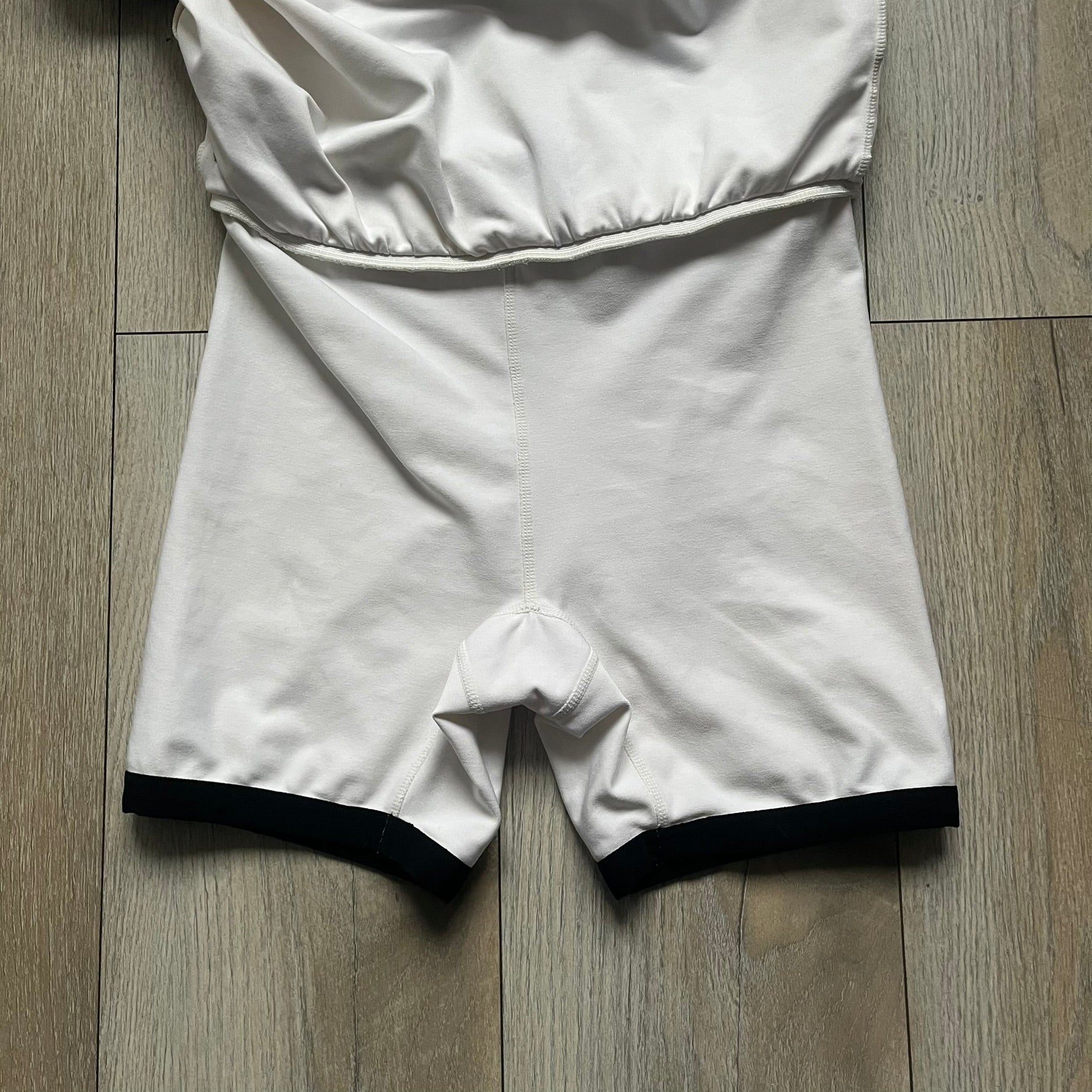 Nike Court Black Trim 90’s Tennis Skirt is a white women’s tennis skort with built-in inner shorts. It features a small Nike Court logo at the lower right hem and black trim detailing along the skirt hem and the bottom of the inner shorts legs.