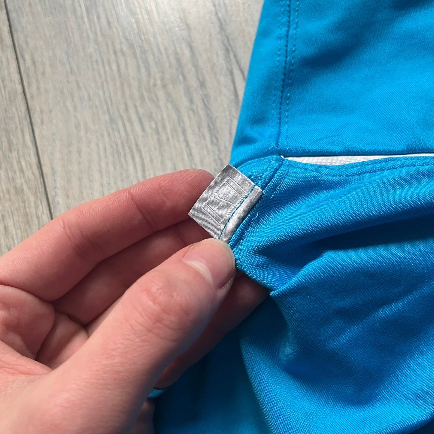 Nike Court Blue Flouncy Tennis Skirt is a women’s tennis skort featuring a built-in inner shorts layer for added coverage and support. The skirt is finished in solid blue with a small white Nike Swoosh at the lower hem and a white contrast line separating the waistband from the main body. A gray Nike Court logo is placed on the side.