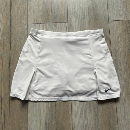 Nike Court Flex Pure Tennis Skirt is a kids’ tennis skort with integrated inner shorts for coverage and support. The skirt is white with a black Nike Swoosh at the lower hem and a Nike Court logo on the opposite side. The front features cut-out sections on both sides for added comfort and mobility.