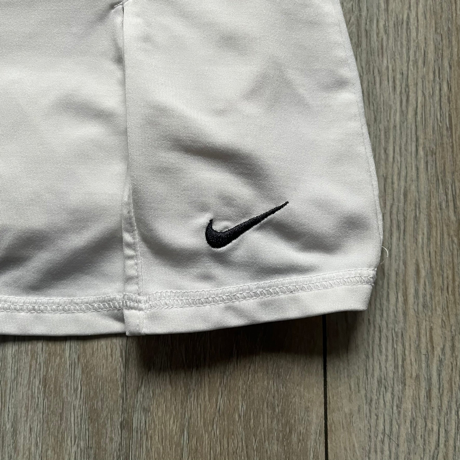 Nike Court Flex Pure Tennis Skirt is a kids’ tennis skort with integrated inner shorts for coverage and support. The skirt is white with a black Nike Swoosh at the lower hem and a Nike Court logo on the opposite side. The front features cut-out sections on both sides for added comfort and mobility.