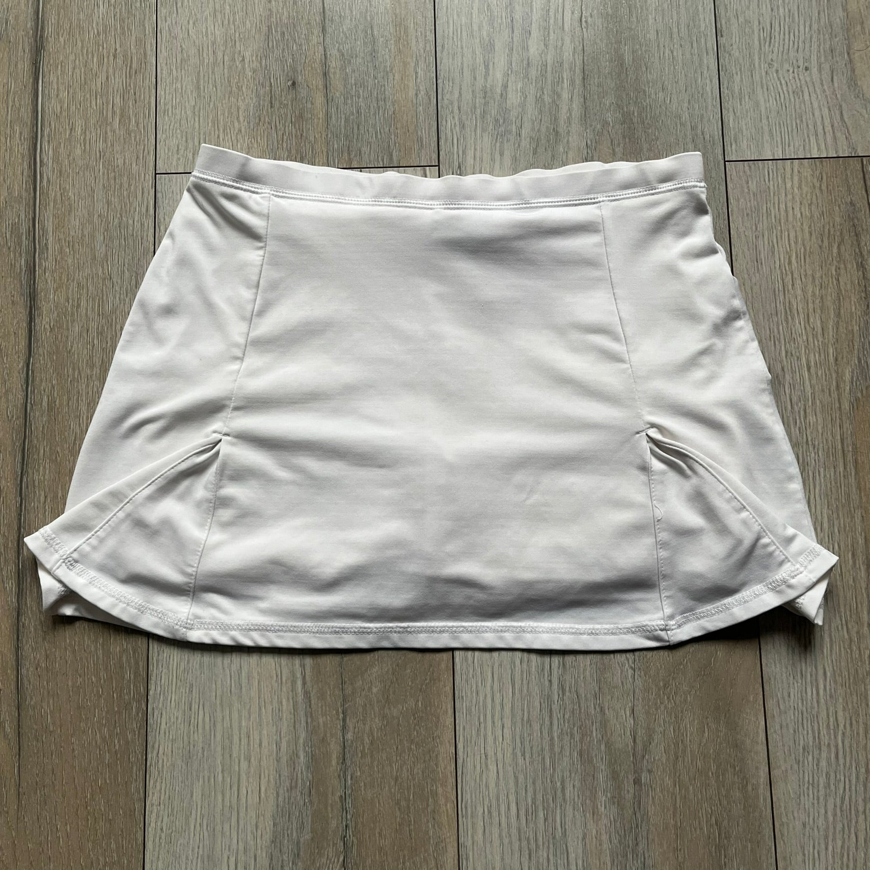 Nike Court Flex Pure Tennis Skirt is a kids’ tennis skort with integrated inner shorts for coverage and support. The skirt is white with a black Nike Swoosh at the lower hem and a Nike Court logo on the opposite side. The front features cut-out sections on both sides for added comfort and mobility.