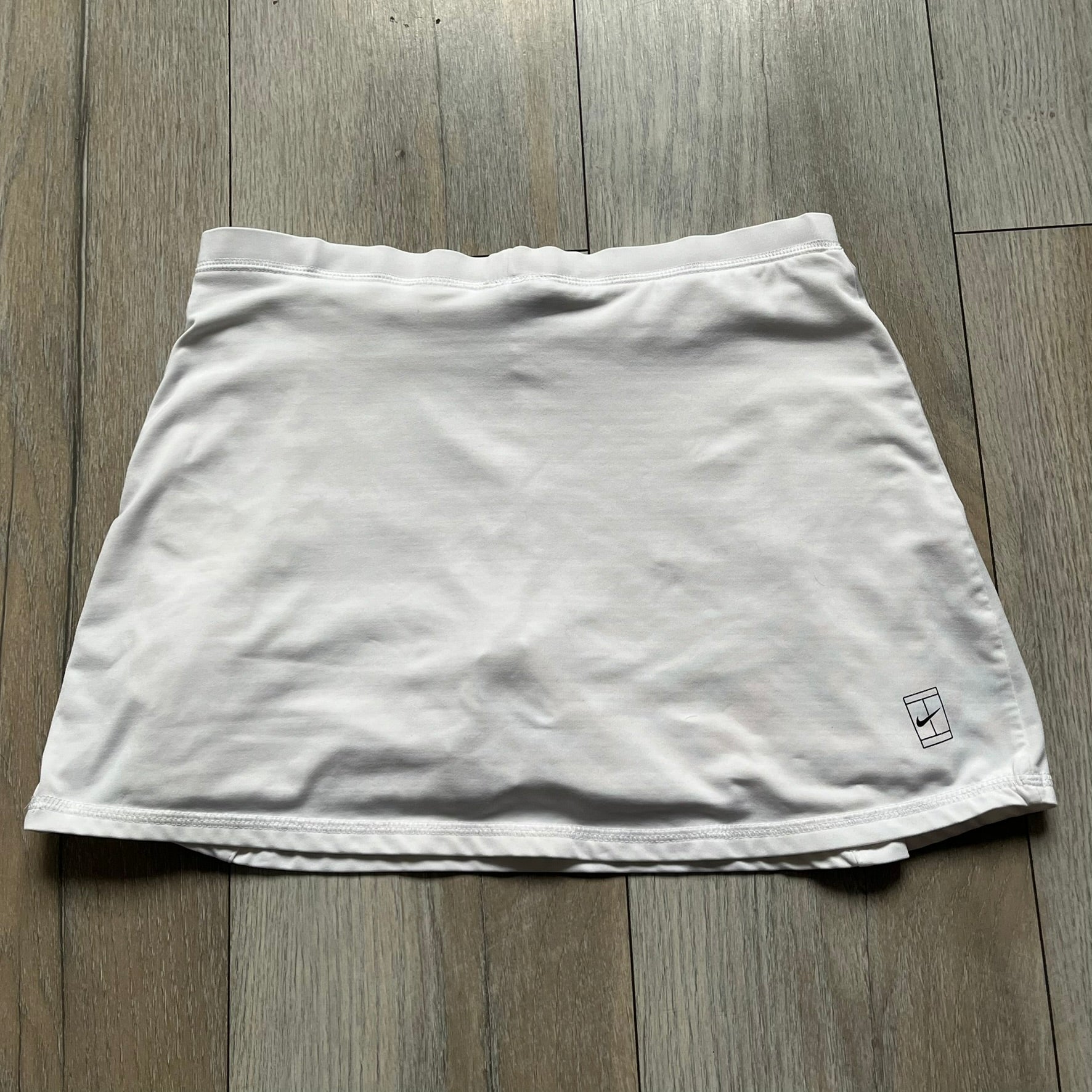 Nike Court Flex Pure Tennis Skirt is a kids’ tennis skort with integrated inner shorts for coverage and support. The skirt is white with a black Nike Swoosh at the lower hem and a Nike Court logo on the opposite side. The front features cut-out sections on both sides for added comfort and mobility.